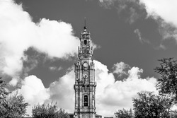 Porto, Portugal: The Clerigos tower; baroque medieval  tower of Clerigos church beyound trees on white clouded sky background in blacck and white