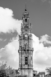 Porto, Portugal: The Clerigos tower; baroque medieval  tower of Clerigos church beyound trees on white clouded sky background in blacck and white