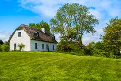 A traditional Irish country cottage house with thatch roof sat next to trees.
