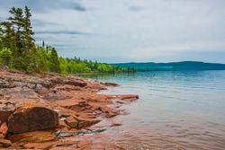 Kama Bay Beach in Nipigon Ontario Canada featuring colorful red and orange rocky shores, lake superior coastal line, overcast sky on summer day