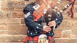 EDINBURGH, SCOTLAND, 24 March 2018 , Scottish bagpiper dressed in traditional red and black tartan dress stand before stone wall. Edinburgh, the most popular tourist city destination in Scotland.