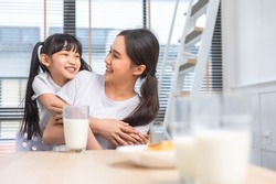 Asian  family enjoying breakfast at living room. little girl daughter sitting on table, drinking milk with smiling father and mother in morning. Happy family at home.
