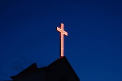 Illuminated cross on a church during blue hour. Christian cross with blue background against the sky. Worshipping concept.