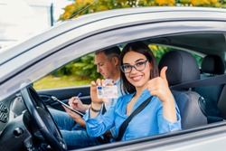 Driving school. Beautiful young woman successfully passed driving school test. She looking sitting in car, looking at camera and holding driving license in hand. Girl with driving license 