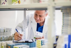 Male pharmacist checking medicines inventory at hospital pharmacy. Pharmacist in drugstore or pharmacy taking notes. Portrait of health care doctor in pharmacy writing on clipboard