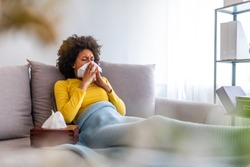 Picture showing sick woman sneezing at home. Young sick woman sneezing in tissue sweating from flu fever. Sick woman catch cold. Sneezing with handkerchief, coughing, got flu, having runny nose. 