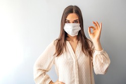 Young woman wearing medical face mask, studio portrait. Woman Wearing Protective Mask and Showing OK sign. Woman wearing surgical mask for corona virus