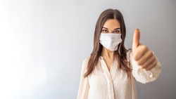 Beautiful caucasian young woman with disposable face mask. Protection versus viruses and infection. Studio portrait, concept with white background. Woman showing thumb up. 