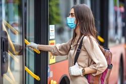 Young female boarding a city bus. Virus pandemic and pollution concept. Woman getting on the bus with protective medical mask and gloves against coronavirus, Covid-2019 