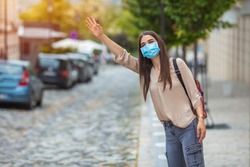 Coronavirus protection. Young woman in the city after the work day, wearing protective mask on the face. Calling for a taxi. Woman wearing mask  while waiting at the busstop after work.