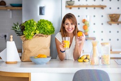 Young woman enjoying fresh orange juice. In her modern kitchen, a woman is about to drink her freshly-made smoothie, which is packed with vitamins. A healthy lifestyle is so much fun.