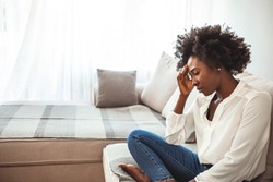 Close up african female sit on couch feels unhappy desperate thinking about personal difficulties mental health problems, 30s sad woman need psychological support goes through divorce break up concept