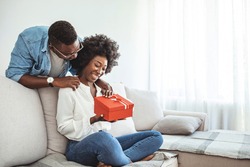 Beautiful young couple is celebrating at home. Handsome man is giving his girlfriend a gift box. Young romantic couple holding present. he guy gives a gift box to his girlfriend.