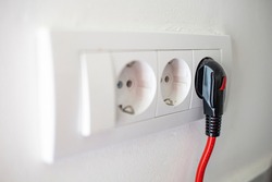 Electric plug. Electric socket. Black power cord cable plugged into european wall outlet on white plaster wall with copy space. 