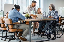 Group of business people in a meeting with colleague in a wheelchair for inclusion. Young businessman greeting handicapped business partner and team. Coworker on wheelchair