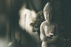 Buddha statue close-up in beautiful light. Close up of a Buddha figurine. Modern decor on a shelf, a buddha and a candle holder and a plants in a pot. Spiritual awakening