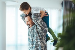 Soldier and his little son hugging at home. Smiling soldier reunited with his son after coming back from war. Military soldier father with son kid smiling during home return - Family love US army