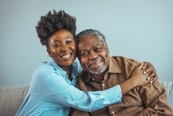 Loving father and daughter together on sofa. Beautiful woman with her father as they both smile. Beautiful young woman embracing her father. Senior African American man and daughter