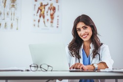 Portrait of female doctor seating in her office at clinic. Friendly Latin American female doctor at the hospital looking at the camera and smiling. Confident female doctor at office desk
