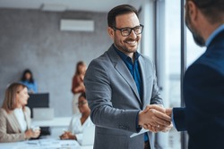 Shot of two businessmen shaking hands in an office. Two smiling businessmen shaking hands while standing in an office. Business people shaking hands, finishing up a meeting