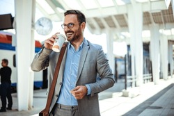 Businessman holding a disposable coffee cup at the train station platform. A man in a train station commuting to work. Businessman with coffee cup. Business person is waiting for train 