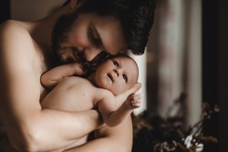 Little baby looks up while bearded man holds her tender