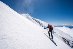 Mountaineer climbs snowfield on a sunny day high on a mountain.