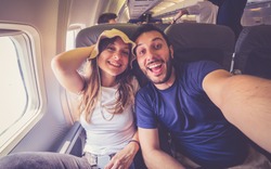 Young handsome couple taking a selfie on the airplane during flight around the world. They are a man and a woman, smiling and looking at camera. Travel, happiness and lifestyle concepts.