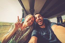 Backpackers traveling around the world on the bus. Young handsome man with his girlfriend on traditional bus taking selfie on smartphone.
