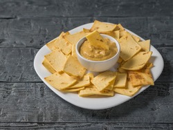 Mexican tortilla chips with cheese and mustard in a clay bowl on a black wooden table. A dish of Mexican cuisine.