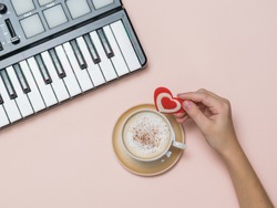 A hand holds a heart figurine near a coffee Cup and a music mixer. The process of creating music. Hobbies and recreation. The view from the top.