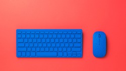 Bright blue keyboard and mouse on a bright red background. Monochrome image of office accessories.