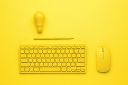 A yellow keyboard with a mouse, a pencil and a light bulb on a yellow background. The concept of business and minimalism. Monochrome.