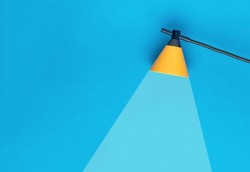 Yellow lamp with a beam of light on a blue background. Minimal business concept. Ray embodying the idea.