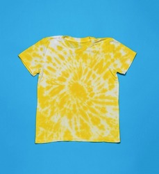 White and yellow T-shirt painted in a spiral tie dye style on a blue background. Minimal fashion concept. Flat lay.