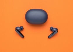 Wireless blue headphones and a closed charging box on an orange background. A popular wireless gadget. Flat lay.