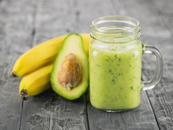 A freshly prepared smoothie of avocado, banana, orange, lemon, parsley and kiwi on a wooden table. Diet vegetarian food.