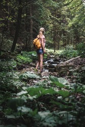 Hiking in forest. Woman with backpack is walking at stream in dark woodland
