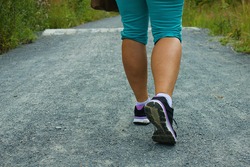 Back view of female legs with sport shoes walking on a gravel trail 
