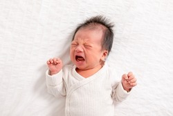 Crying and angry Newborn baby boy lying on white bed at home.Infant baby screaming very hungry or stomach pain.sick asian baby crying and having fever.Tired baby crying concept