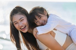 Happy asian mom holding her daughter playing together on the beach with fresh air.happy outdoor little girl hugging mother smile and love having fun enjoy with sunset on the beach.Mother day concept