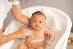 Adorable of asian newborn baby bathing in bathtub.mother bathing her son in warm water.Happy adorable newborn infant smile in tub relax and comfortable.Newborn baby care concept
