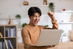 Asian man is smiling and expressing happy feeling on the computer laptop screen. young male got good news and show his cheerful face.Happiness men looking on laptop read message feel excited at home