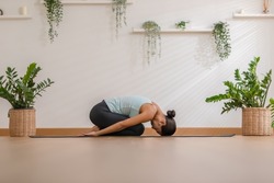 Side view of Asian woman wearing green sportwear doing Yoga exercise,Yoga Child’s pose or Balasana,Calm of healthy young woman breathing meditation with yoga at home,Exercise for wellness life