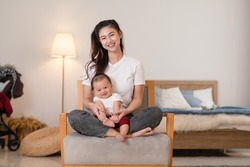 Happy asian mom playing and spending time with her newborn baby and looking at camera together at home. Adorable baby boy smile laughing with mother in warmth place relax and comfortable.good moment