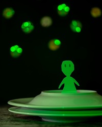 A funny green alien cut out of cardboard is on a spaceship made with two overlapping plates