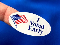 I voted early sticker on woman’s finger with blue fabric background