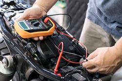 mechanic using multimeter to check the voltage level on motorcycle battery at motorcycle garage, Maintenance and repair concept