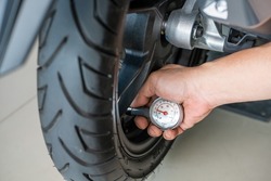 Hand holding portable tire pressure gauge checking air pressure for  motorcycle tire.  maintenance, repair motorcycle concept in garage .selective focus