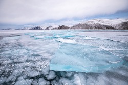 Surreal frozen winter landscape of blue multi-layered ice on lake Baikal on a cloudy day. Lake Baikal, Siberia, Russia.